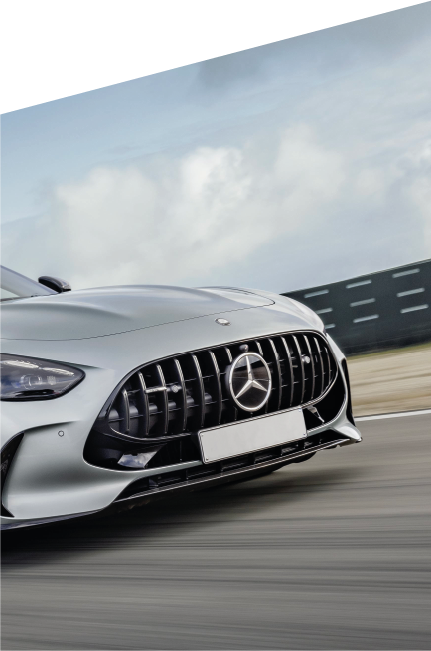 Dettaglio frontale di una Mercedes-AMG in movimento su pista, con griglia Panamericana nera lucida, sfondo sfocato e cielo nuvoloso.