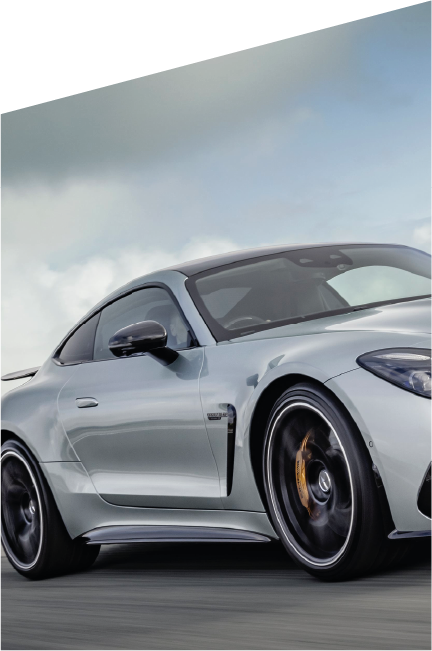 Vista laterale di una Mercedes-AMG color grigio opaco in corsa su pista, con cerchi sportivi neri e pinze freno dorate, sotto un cielo nuvoloso.