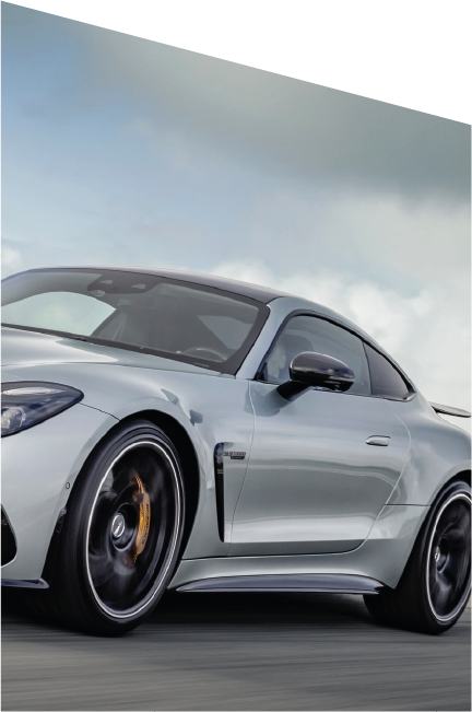 Dettaglio laterale sinistro di una Mercedes-AMG grigia in movimento su strada, con cerchi sportivi neri e pinze freno dorate, sotto un cielo nuvoloso.