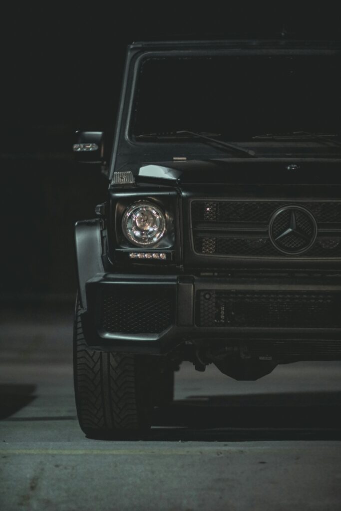 Mercedes-Benz Classe G nera in un parcheggio notturno, vista frontale con faro acceso e design squadrato tipico del SUV premium tedesco.